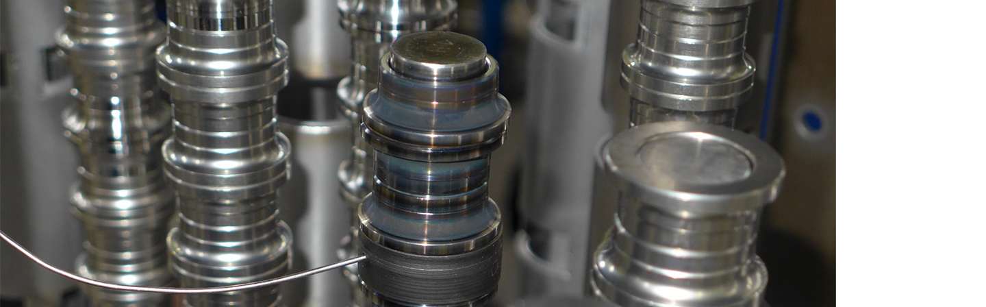 Structure of a sample batch with towers of bearing rings: In the foreground, inner rings mounted on a core rod with thermal-element feed into a measuring element; in the background and on the right are outer rings.