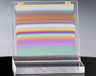 A transparent element displays a series of colorful horizontal stripes in soft shades such as blue, green, yellow, orange, and pink, which gently blend into one another. The background is bright and blurred, making the colors of the object stand out more.